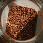 Top view of a jar filled with instant coffee granules, illuminated by sunlight.